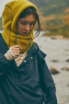 a woman wearing a yellow hoodie is standing by the water and looking down at her cell phone