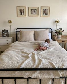 a small child is sitting on a bed with white sheets and pillows, looking at the camera