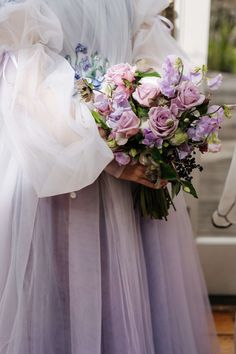 a woman holding a bouquet of flowers in her hand and wearing a dress with sheer sleeves