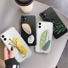 four iphone cases sitting on top of a white table next to a cup of coffee