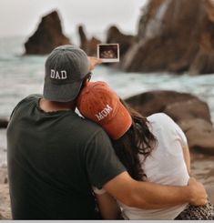 a man and woman sitting on the beach taking pictures