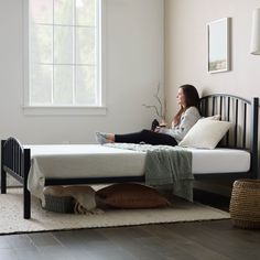 a woman sitting on top of a bed next to a white rug and window in a room