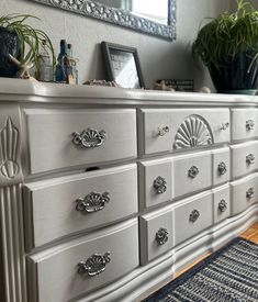 a white dresser with silver handles and knobs next to a potted houseplant