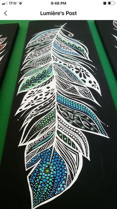 two black and green paintings with white designs on them, one has a blue feather painted on it