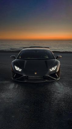 a black sports car parked in front of the ocean at sunset with its lights on