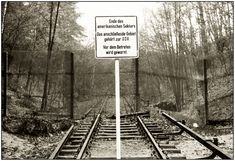 black and white photograph of train tracks with a sign in the foreground that says,