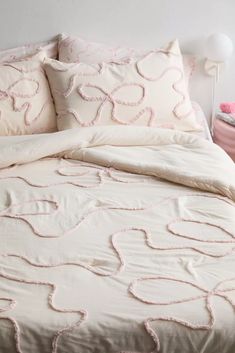 a bed with white and pink comforters in a bedroom area next to a nightstand