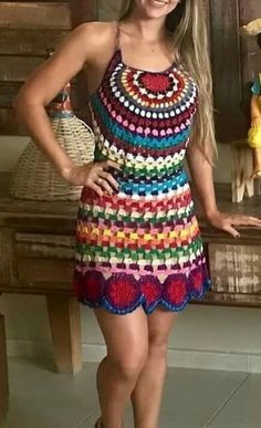 a woman standing in front of a wooden bench wearing a multicolored crochet dress