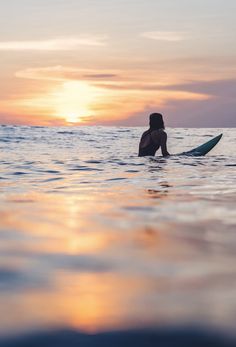 a person sitting on a surfboard in the ocean at sunset or dawn with their back turned to the camera
