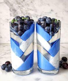 two glass vases filled with blueberries and other berries on a table next to marble