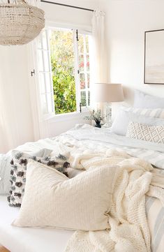 a bed with white sheets and pillows on top of it in a bedroom next to a window