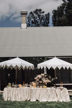 two white umbrellas sitting on top of a table covered in flowers and fruit next to a building