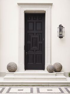 a black door with two stone balls in front of it and a light on the wall