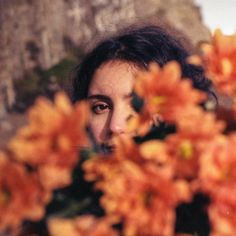 a woman is looking at the camera through some flowers