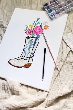 a drawing of a boot with flowers on it next to a paintbrush and watercolor palette