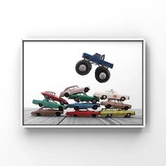 an art piece with cars and monster trucks in the air above it is a white wall