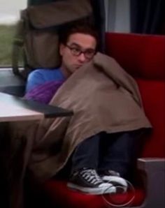 a man sleeping on a train with his head under a blanket