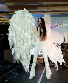 a woman in white pants and angel wings on stage