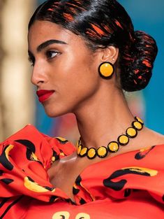 a woman in an orange dress with black and yellow designs on her neck, wearing large earrings