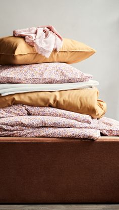 a pile of pillows sitting on top of a brown bed next to a white wall