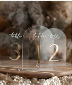 three clear acrylic table numbers sitting on top of a wooden board with glitter around them