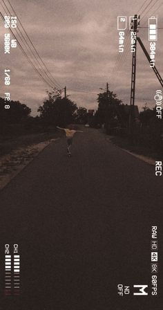 a person walking down the middle of an empty street with power lines above them and telephone poles in the distance