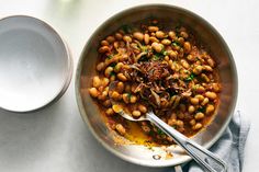 a bowl filled with beans and onions next to a spoon on top of a table