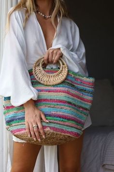 a woman in white shirt holding a straw bag with multicolored stripes on it