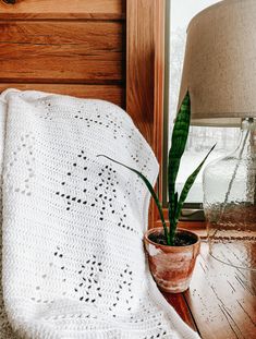 a potted plant sitting on top of a wooden table next to a white crocheted blanket