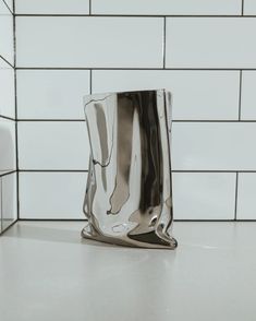 a silver vase sitting on top of a counter next to a white tile backsplash