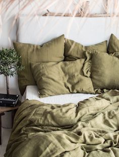 an unmade bed with green sheets and pillows on top of it next to a potted plant