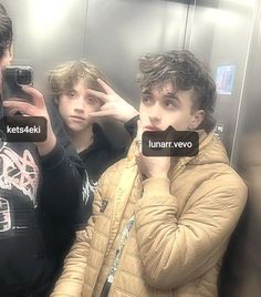 three young men are taking selfies in the bathroom mirror, one is holding his cell phone up to his ear