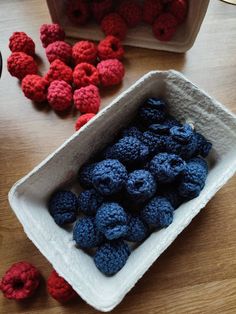 some raspberries are in a white bowl on a wooden table next to other berries