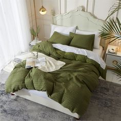 a bed with green comforter and pillows in a room next to a plant on the floor