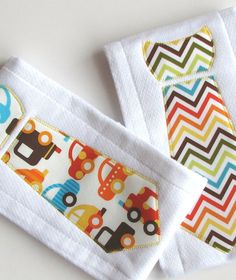 two baby bibs with cars and trucks on them sitting next to each other in front of a white background