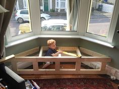 a young boy sitting on top of a wooden bed in front of a large window