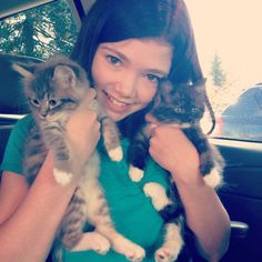 a woman holding two kittens in her arms while sitting in the back seat of a car