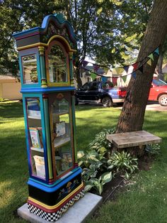 a colorful clock sitting in the grass next to a tree