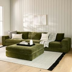 a green couch and ottoman in a living room with white walls, rugs and wood flooring