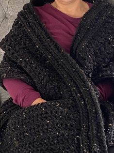 a woman wearing a black crocheted shawl sitting on a couch with her arms crossed