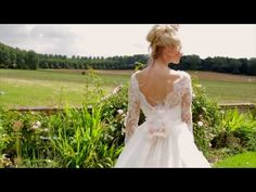 a woman wearing a wedding dress standing in front of a lush green field with flowers