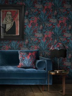 a blue couch sitting in front of a painting on a wall next to a lamp