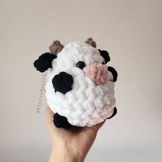 a hand holding a small crocheted cow ornament in white and black