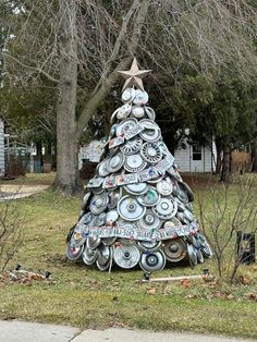 a christmas tree made out of plates and pans in front of a house with a star on top