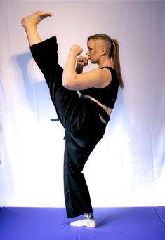 a woman in black pants doing a kickbox pose on a blue mat with her leg up