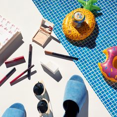 various items laid out on top of a blue and white table with sunglasses, eyeliners, lipstick, an inflatable doughnut