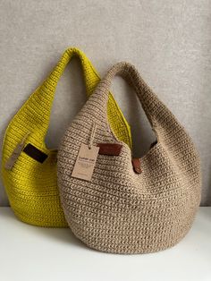 two knitted purses sitting next to each other on a white counter top, one yellow and the other brown