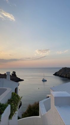 a boat is out in the water near some white buildings and cliffs at sunset or dawn