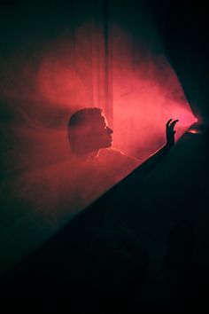 the silhouette of a person in front of a red and black light with their hand up