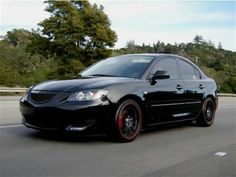 a black car driving down the road with trees in the backgrounds